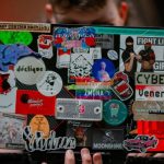 Remarketing Ppc - A man holding a laptop with a bunch of stickers on it