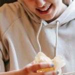 Shareable Content - Smiling plump female wearing comfy hoodie eating crispy yummy potato chips while sitting in light room