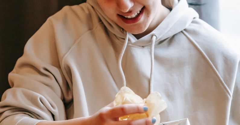 Shareable Content - Smiling plump female wearing comfy hoodie eating crispy yummy potato chips while sitting in light room