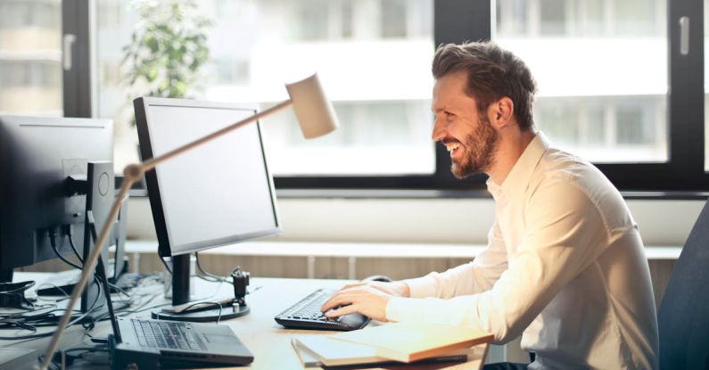 Email Metrics - Man in White Dress Shirt Sitting on Black Rolling Chair While Facing Black Computer Set and Smiling