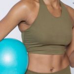 Content Recycling - Cheerful African American lady in activewear with blue ball drinking orange juice and looking at camera against white background