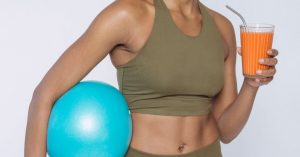 Content Recycling - Cheerful African American lady in activewear with blue ball drinking orange juice and looking at camera against white background