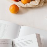 Product Page - Jute sack with appetizing ripe apricots placed on table with different books